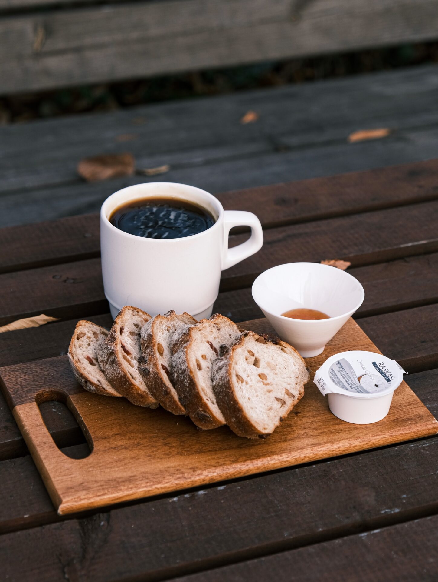 A cup of coffee, cream, and several slices of bread are displayed on a wooden serving tray