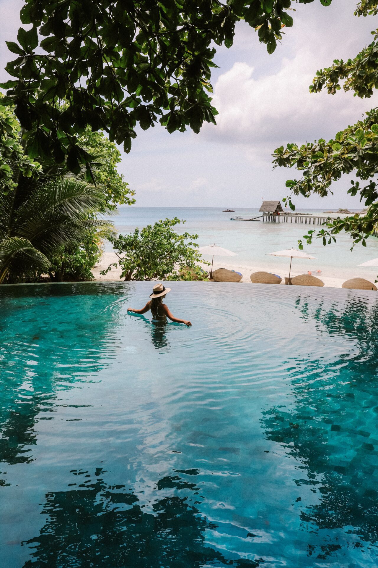 Person stands in infinity pool looking out at a tropical beach