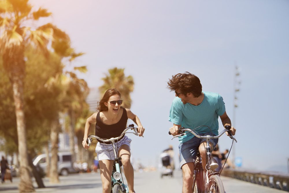 Happy young woman chasing man while riding bicycle on a sunny day